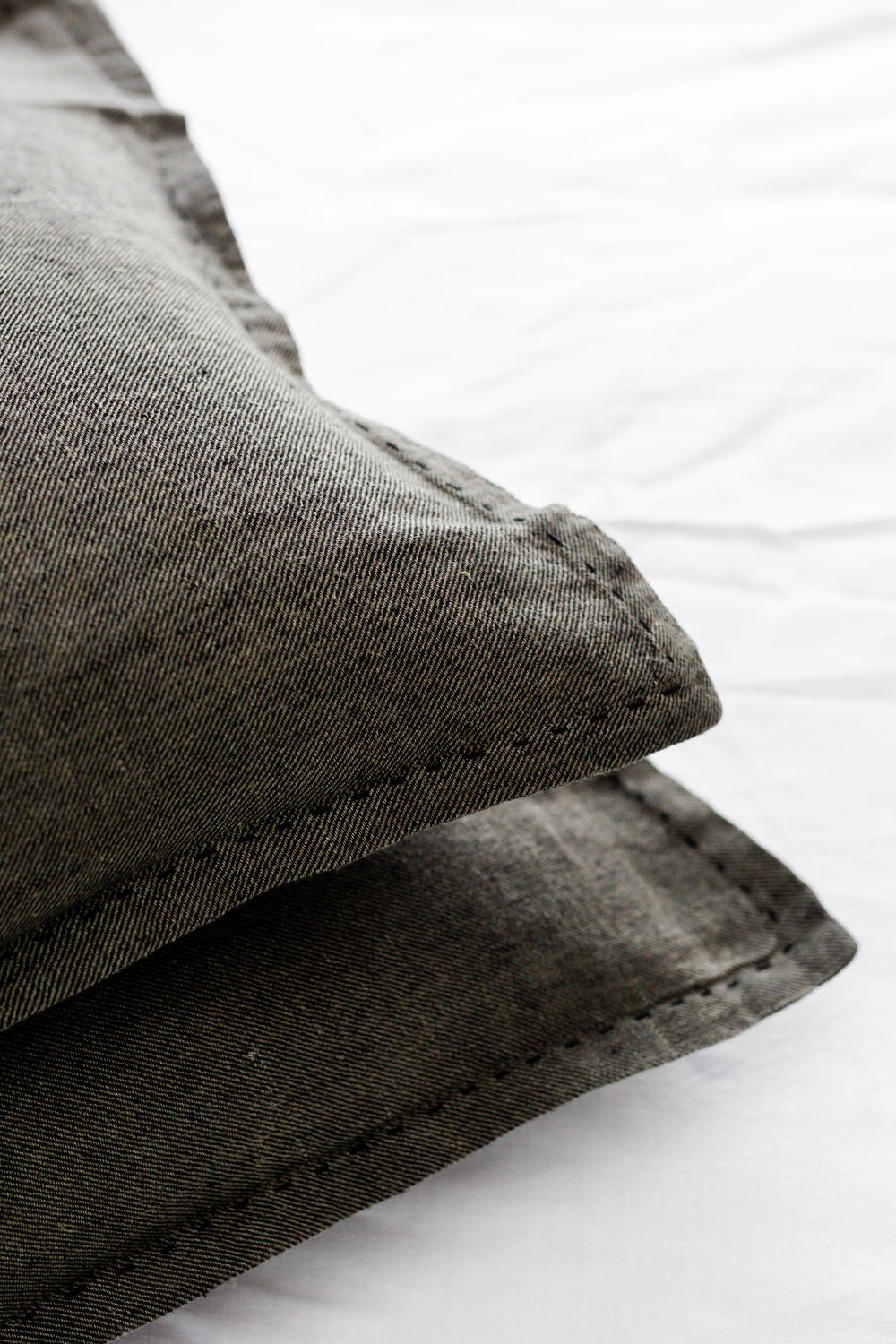 Close-up of a gray denim pillow with visible stitching on a white surface.