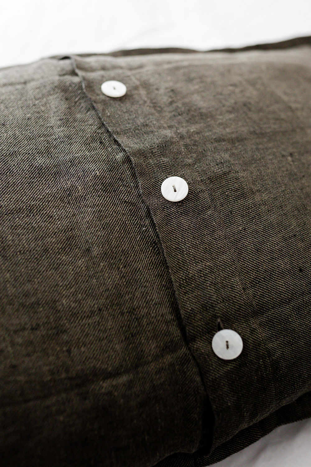 Close-up of a dark denim shirt with a vertical seam and white buttons.