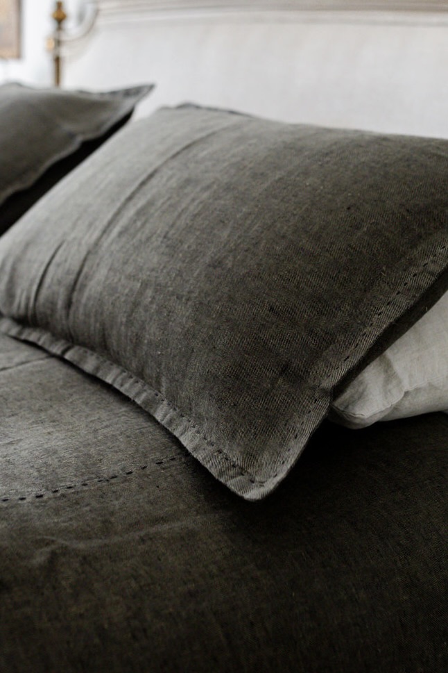 Close-up of a dark gray pillow resting on a bed with matching gray sheets, showing textured fabric detail.