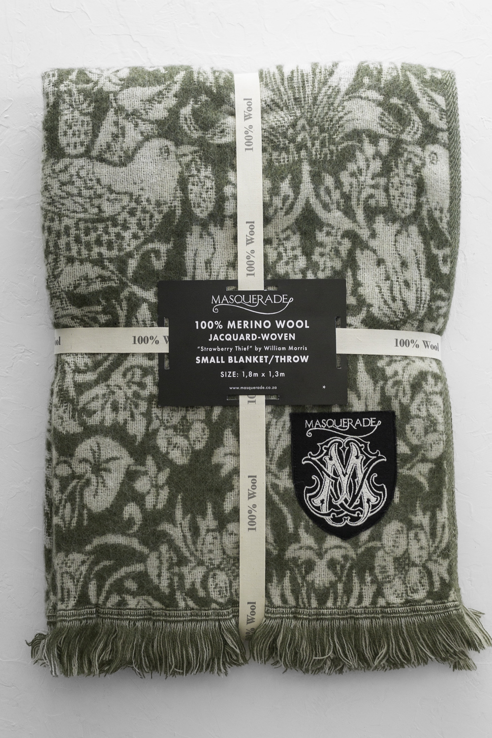 Jacquard-woven green and beige merino wool throw with fringed ends, Masquerade label and crest patch